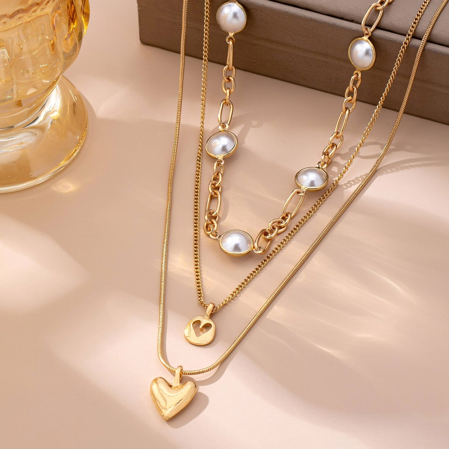 Gold necklaces with heart and pearl pendants on a beige surface