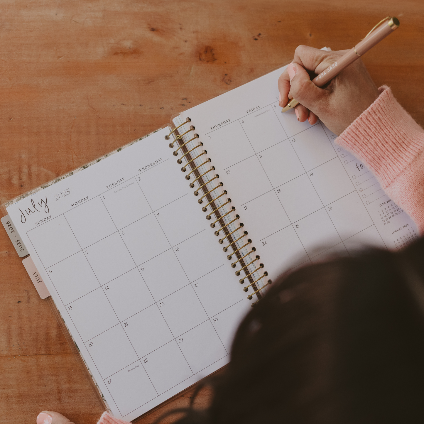 Person holding a pen over a calendar on a wooden surface