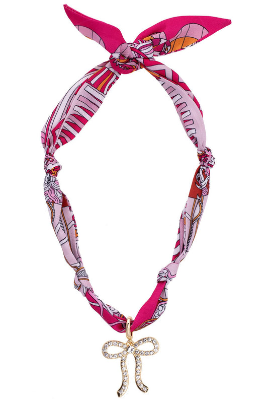 Pink and white patterned headband with a decorative bow charm on a white background