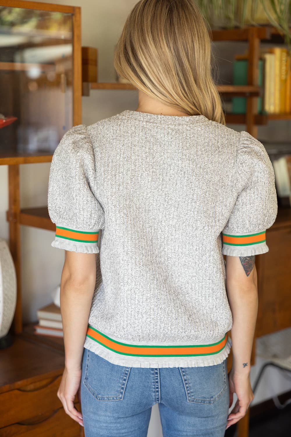 Person wearing a light gray short-sleeve shirt with colorful trim in an indoor setting.