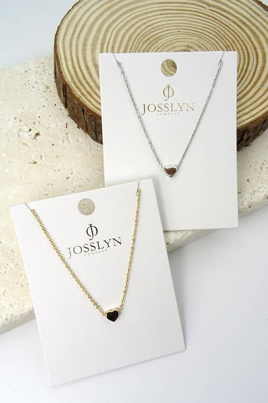 Two necklaces on display cards with 'Josslyn' branding against a natural wood and stone background.