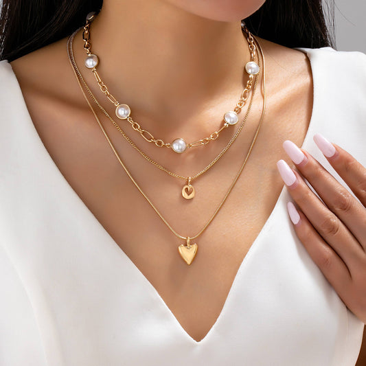 Woman wearing multiple gold necklaces with heart pendants on a plain background