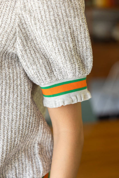 Close-up of a person wearing a textured sweater with a colorful band on the sleeve.