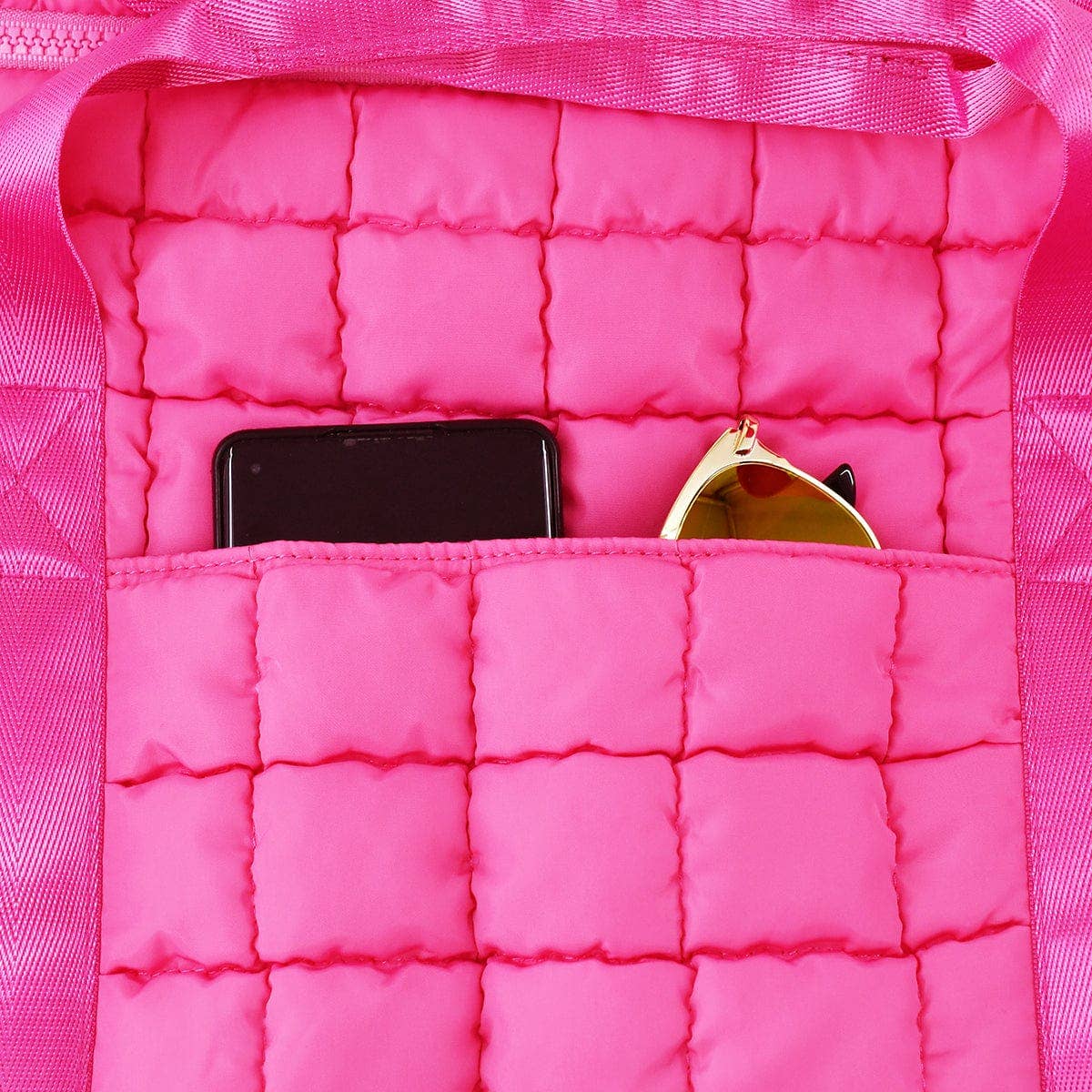 Close-up of a pink quilted bag with a phone and sunglasses inside.