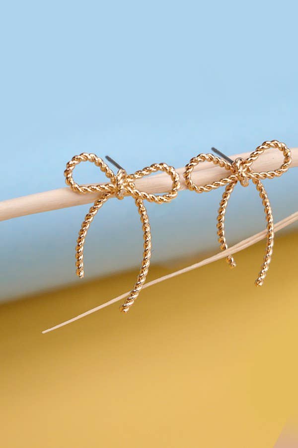 Gold bow-shaped earrings on a stick against a blue and yellow gradient background