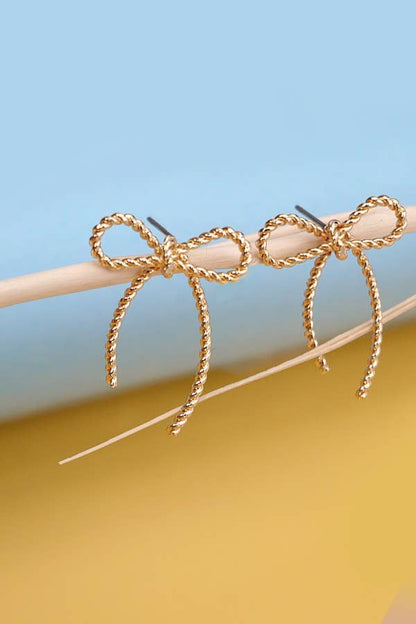 Gold bow-shaped earrings on a stick against a blue and yellow gradient background