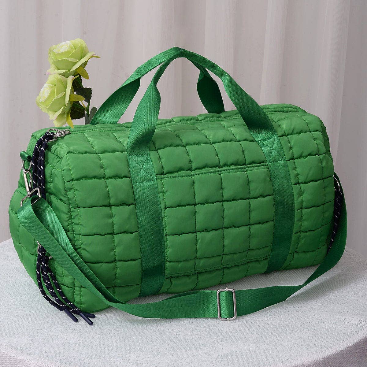 Green quilted duffel bag with a strap on a light background