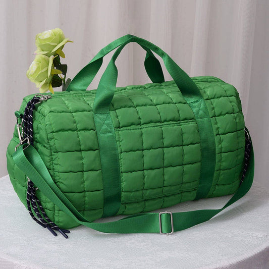 Green quilted duffel bag with a strap on a light background