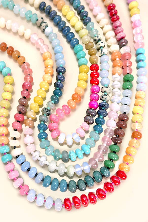 A set of multiple colorful beaded strands arranged in overlapping curved rows on a light cream background. The beads come in many different colors and stone-like finishes, including pink, yellow, blue, green, red, white, and brown.