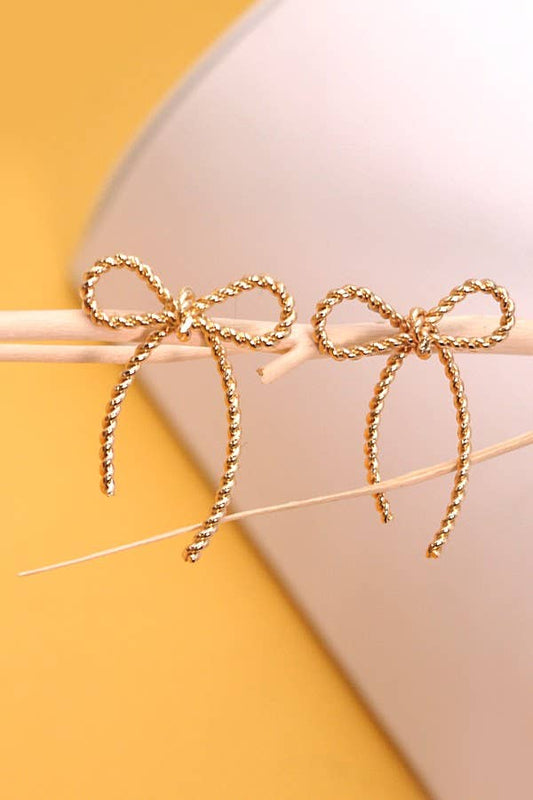 Gold bow-shaped earrings on a yellow and beige background