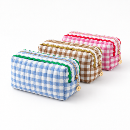 Three small zippered pouches with gingham checks are arranged on a white background. The front pouch is light blue and white with a green stitched trim and gold zipper.