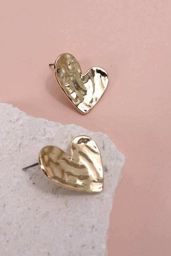 Gold heart-shaped earrings on a stone surface with a pink background