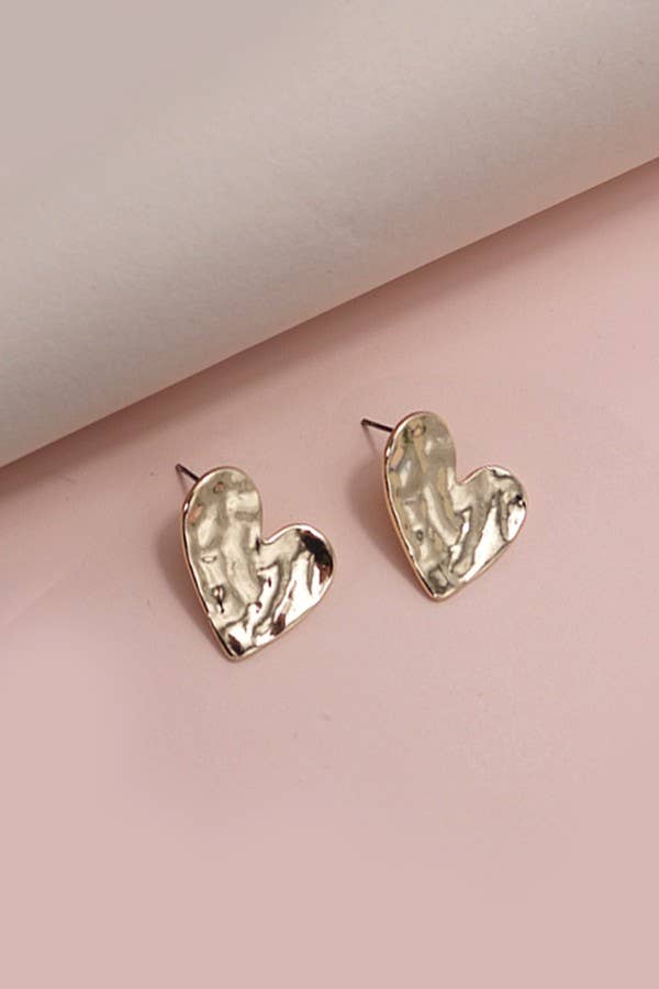 Gold heart-shaped earrings on a pink background