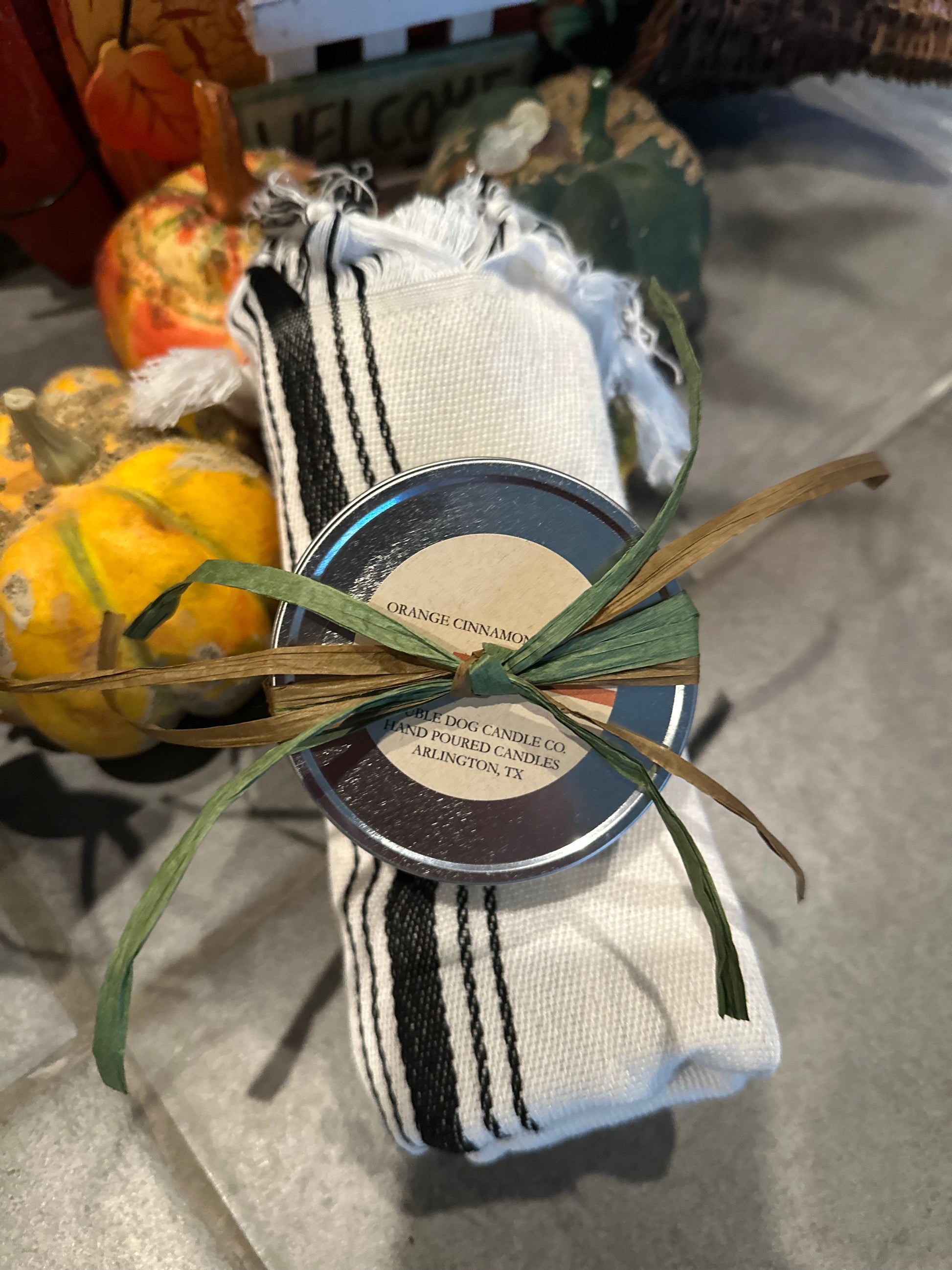 Small container wrapped in white cloth with black stripes and a green ribbon, set against a neutral background.