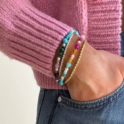 Close-up of a hand wearing colorful beaded bracelets on a pink sweater background