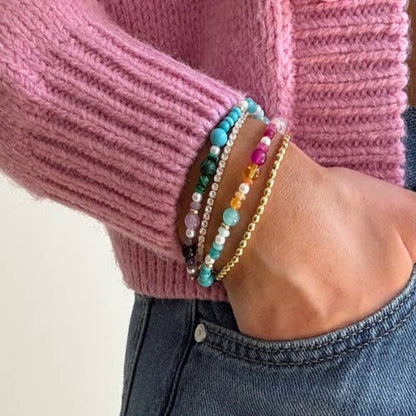 Close-up of a hand wearing colorful beaded bracelets on a pink sweater background