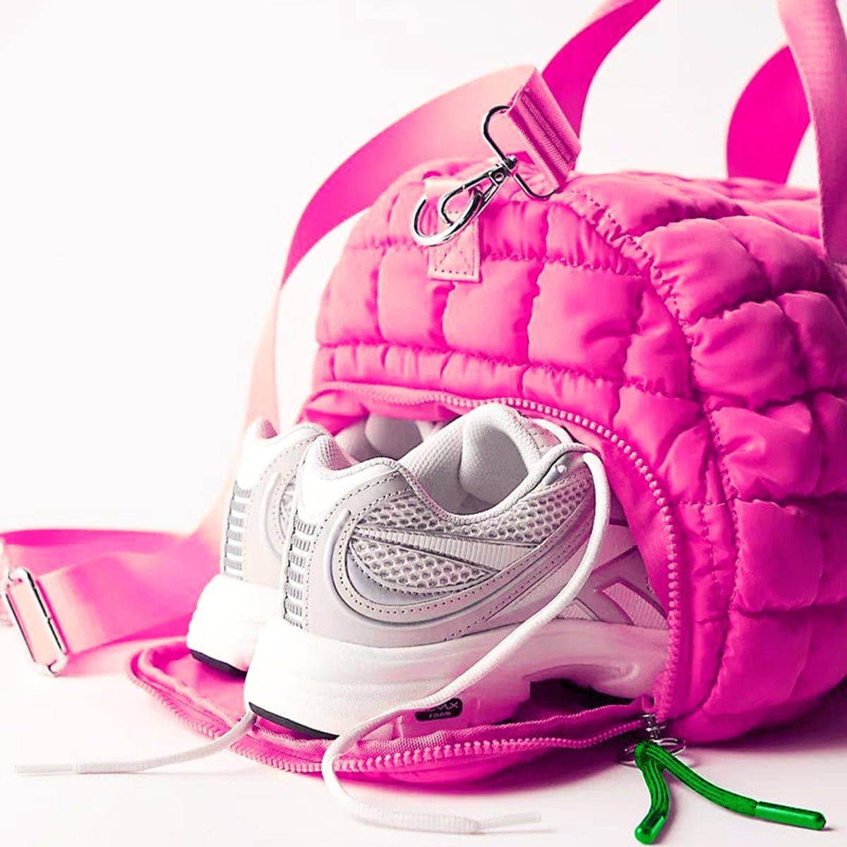Pink quilted handbag with a white sneaker inside on a white background