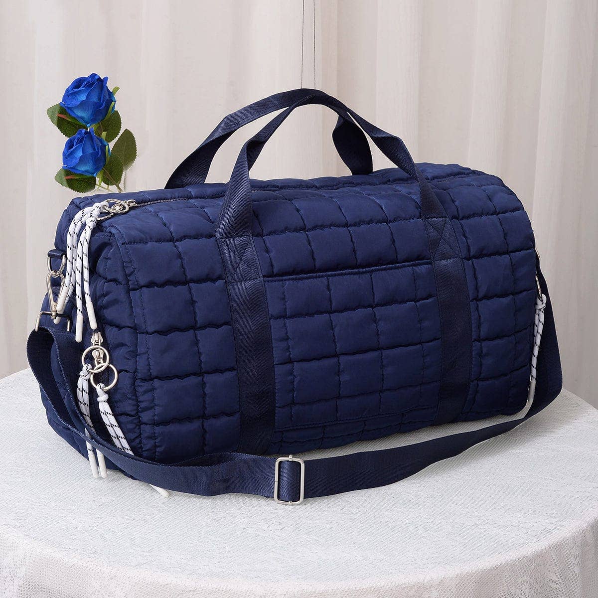 Navy blue quilted duffel bag with decorative elements on a white surface.